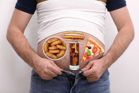 Man wearing tight t-shirt and jeans with images of different unhealthy food on his belly against...