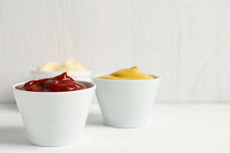 Ketchup, mustard and mayonnaise in bowls on white table, space for textの写真素材
