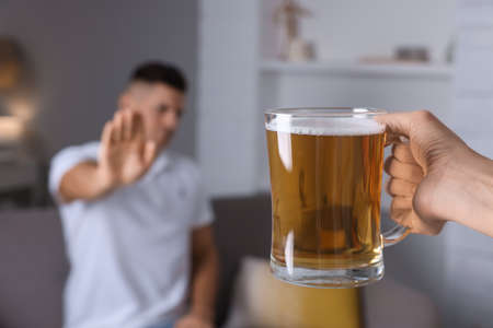 Man refusing to drink beer in kitchen, closeup. Alcohol treatment addictionの写真素材