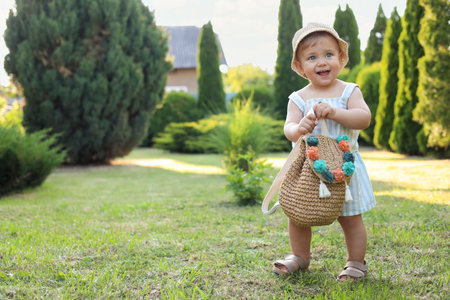 Cute little girl in stylish clothes with knitted backpack outdoors on sunny day. Space for textの写真素材