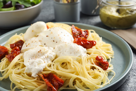 Delicious spaghetti with burrata cheese and sun dried tomatoes on gray table, closeupの写真素材