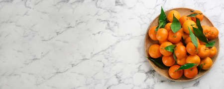 Fresh ripe tangerines and green leaves on white marble table, top view with space for text. banner designの写真素材