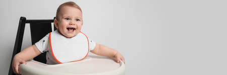 Cute little baby wearing bib in highchair on white background, space for text. banner design