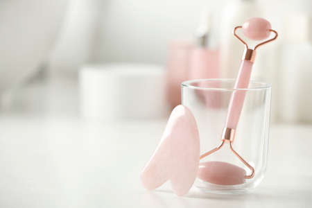 Natural face roller and gua sha tool on white table against blurred background, closeup. Space for...