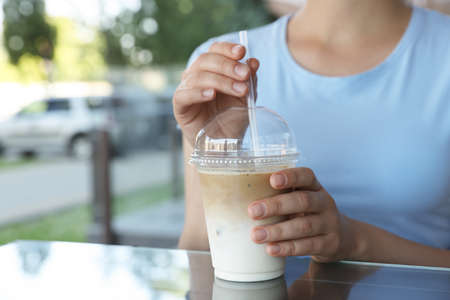 Woman with plastic takeaway cup of delicious iced coffee at table in outdoor cafe, closeupの写真素材