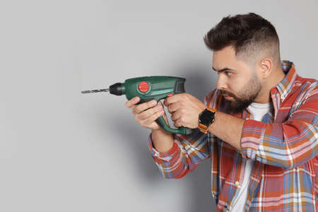 Young man with power drill on gray background