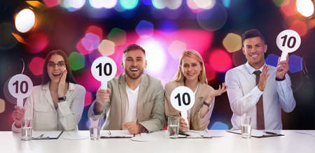 Panel of judges holding signs with highest score at table against blurred background. bokeh effect