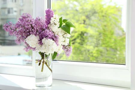 Beautiful lilac flowers in glass vase on windowsill. Space for textの写真素材