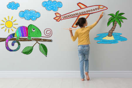 Cute child girl painting plane on light gray wall indoorsの写真素材