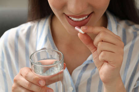 Young woman with glass of water taking dietary supplement pill, closeupの写真素材
