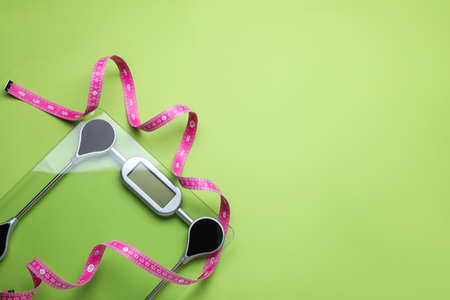 Electronic scales and measuring tape on green background, flat lay. Space for text