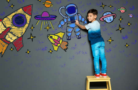Cute child boy draws space with chalk on gray wallの写真素材