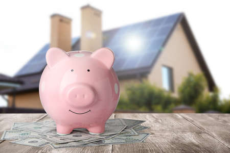 Piggy bank and money on wooden surface and blurred view of beautiful house, space for text. Mortgage conceptの写真素材