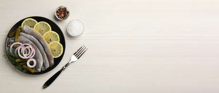 Salted herring fillets served with onion rings, pickles, dill and lemon on light beige wooden table, flat lay with space for text. banner designの写真素材