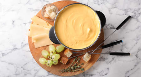 Flat lay composition with pot of delicious cheese fondue on white marble table. banner designの写真素材