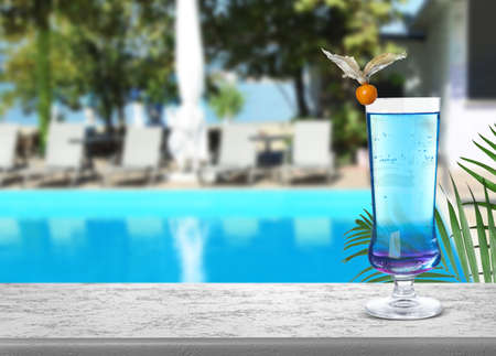 Tasty refreshing cocktail on light gray stone table near outdoor swimming pool, space for textの写真素材