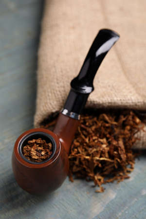 Smoking pipe, dry tobacco and sackcloth on blue wooden table, closeup