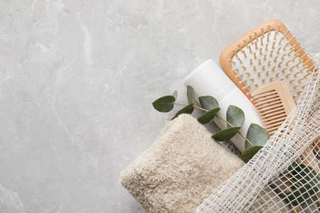 Dry shampoo spray, towel and hairbrushes with eucalyptus branch on light gray table, top view. Space...