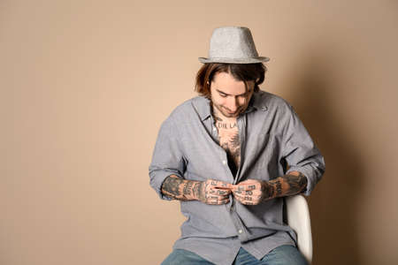 Young man with tattoos on body against beige background