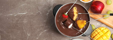 Flat lay composition with chocolate fondue in pot and fruits on brown marble table, space for text. banner designの写真素材