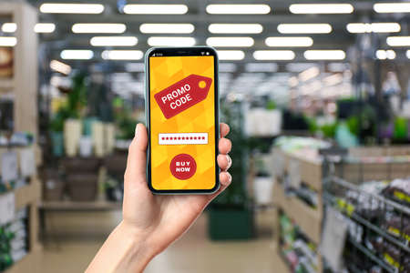 Woman holding smartphone with activated promo code in gardening store, closeupの写真素材