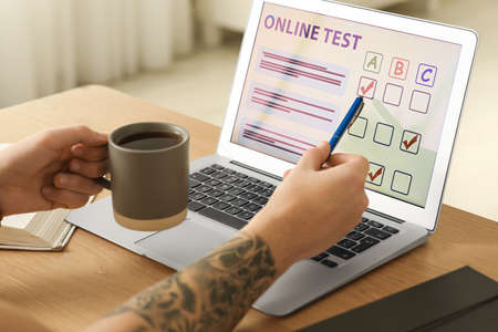 Man taking online test on laptop at desk indoors, closeup