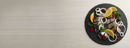 Slate plate with sliced salted herring fillet, parsley, chili pepper, onion rings and lemon on light...
