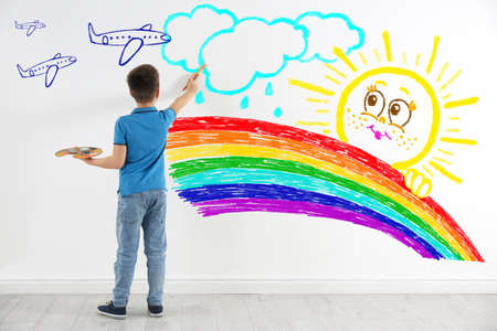 Cute child boy drawing of colorful dye on white wall indoorsの写真素材