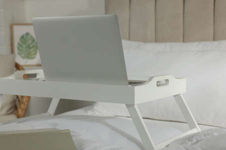 White tray with modern laptop and smartphone on bed indoors