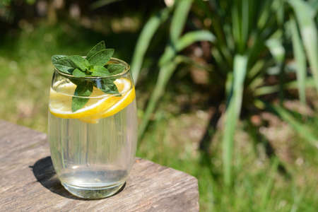 Refreshing water with lemon and mint on wooden table outdoors, space for text
