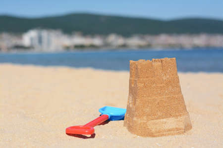 Sand castle and child plastic shovel on beach near sea. Space for text