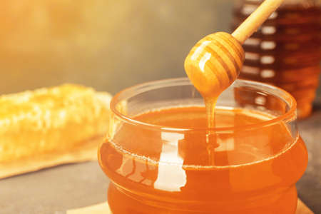 Sweet drip honeyping from dipper into glass jar, closeupの写真素材