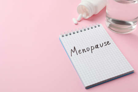 Notebook with word Menopause near pills and glass of water on pink background, space for textの写真素材