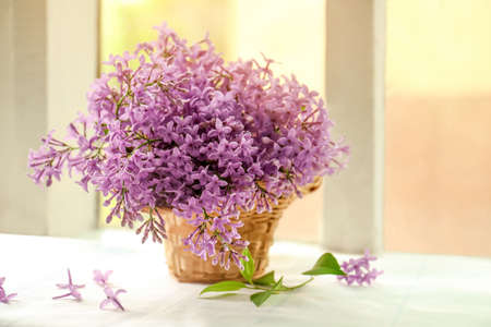 Beautiful lilac flowers in wicker basket on window sill indoorsの写真素材