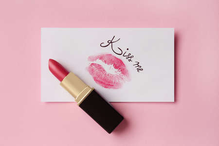 Paper card with lip print, phrase Kiss Me and lipstick on pink background, top viewの写真素材