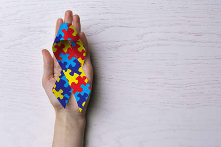 World Autism Awareness Day. Woman with colorful puzzle ribbon on white wooden background, top view...