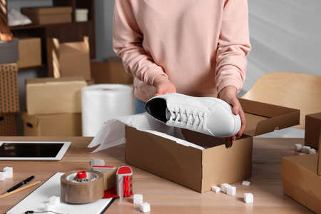 Seller packing shoes into cardboard box at table in office, closeup. online store