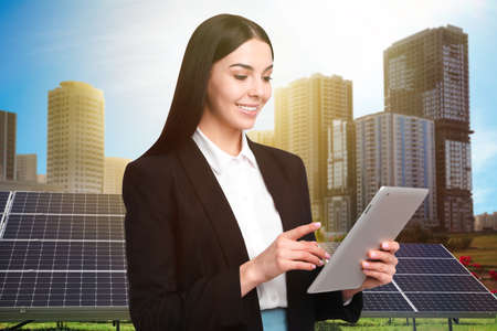 Young businesswoman with tablet near solar panels and beautiful view of cityscape. alternative energy sourcesの写真素材