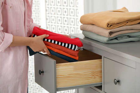 Woman putting clean clothes into drawer at home, closeup