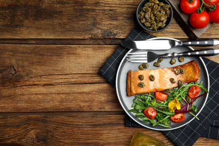 Tasty cooked salmon with capers and salad served on wooden table, flat lay. Space for textの写真素材