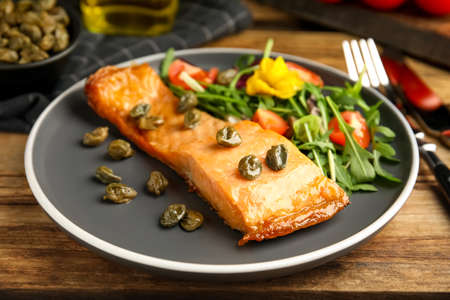 Tasty cooked salmon with capers and salad served on wooden table, closeupの写真素材