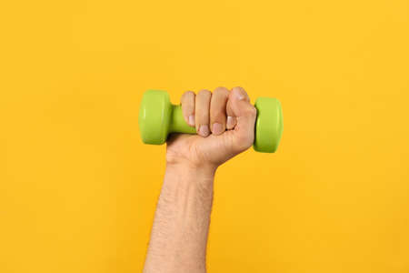 Man holding dumbbell on orange background, closeupの写真素材