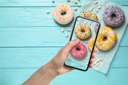 Woman taking picture of tasty donuts on light blue wooden table, top view