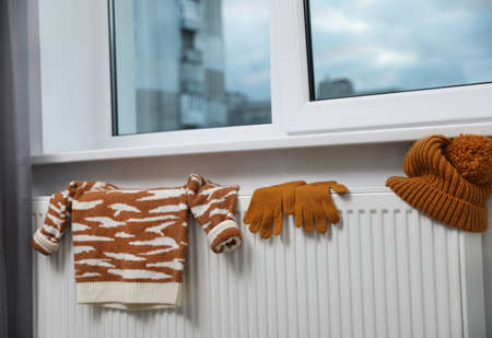 Knitted hat, sweater and gloves on heating radiator near window indoorsの写真素材
