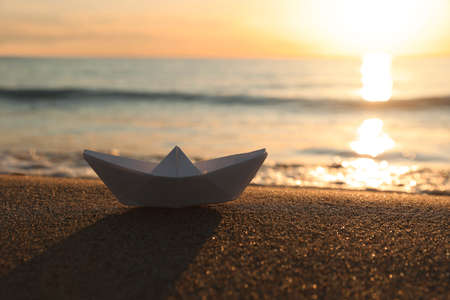 White paper boat on sand near sea at sunset, space for textの写真素材