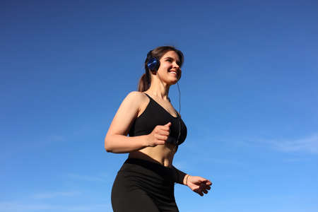 Young woman listening to music while running outdoors in the morning, low angle viewの写真素材