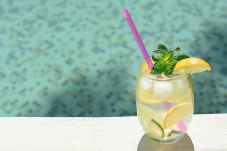 Refreshing drink with citrus slices and mint near swimming pool. Space for text