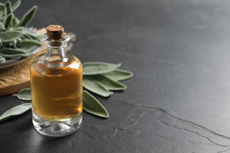 Bottle of essential sage oil and leaves on black table. Space for textの写真素材