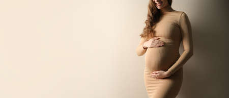 Pregnant woman touching her belly on beige background, space for text. banner designの写真素材