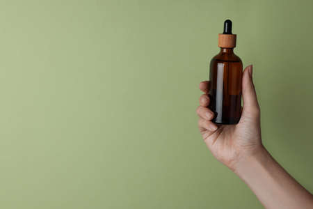 Woman holding bottle of cosmetic product on pale olive background, closeup. Space for textの写真素材